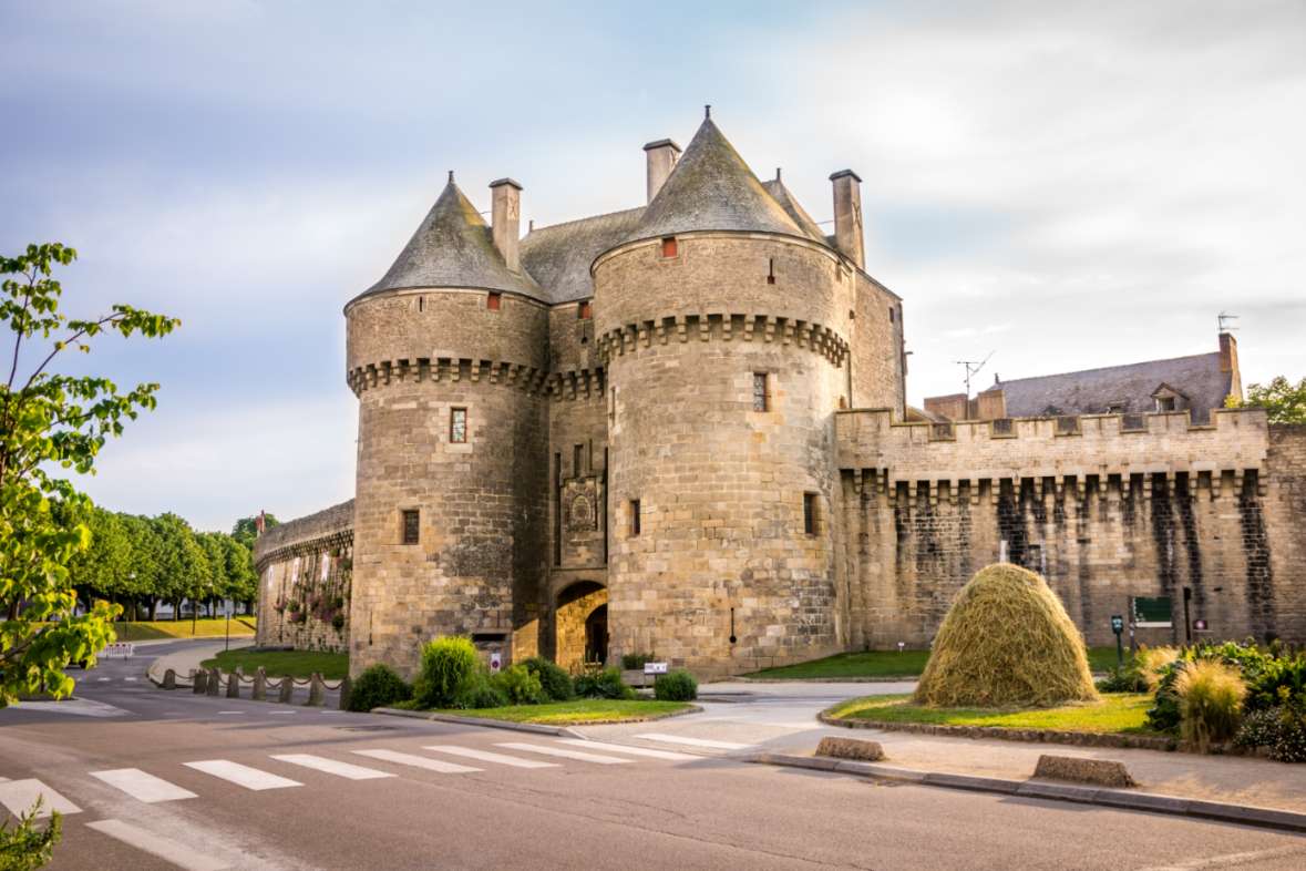 Façade extérieure d'un château médiéval en pierre avec deux tours d'enceinte et un passage voûté