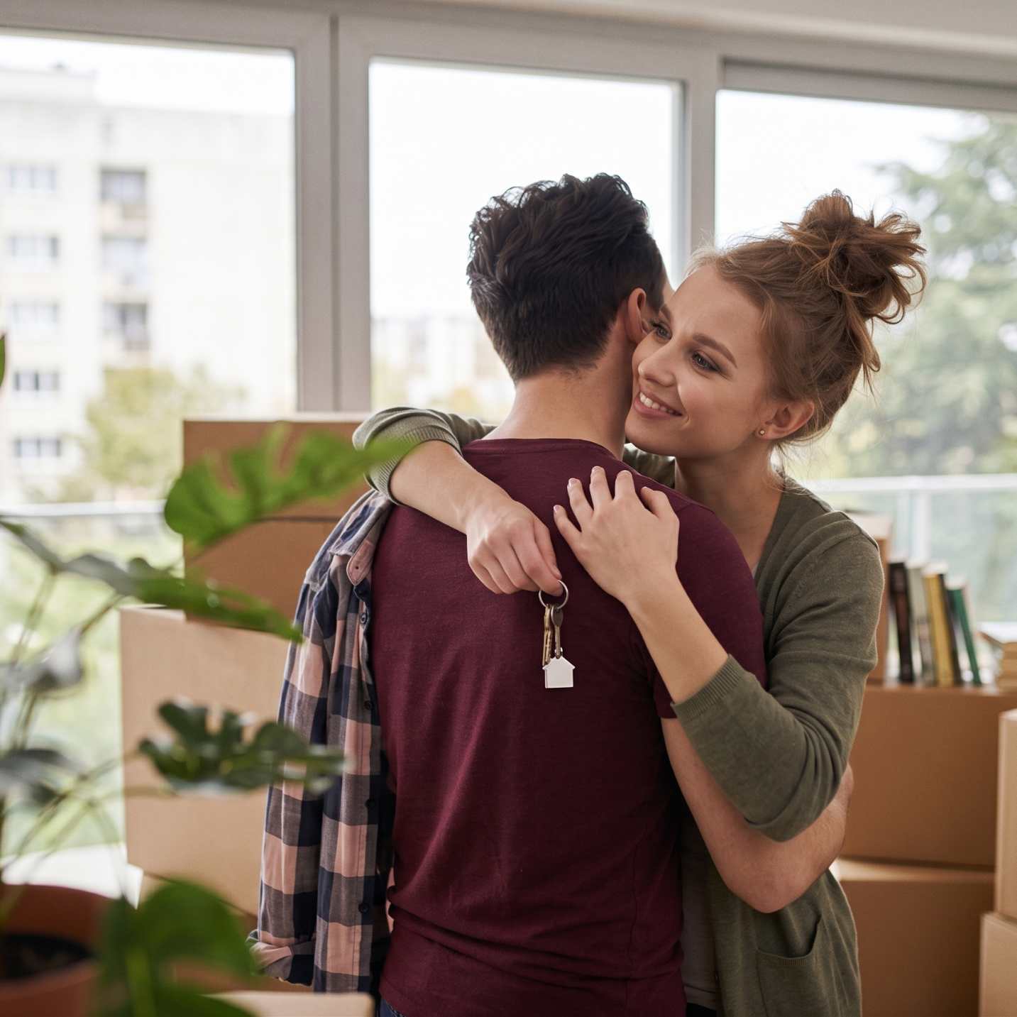 Jeune couple s'embrassant avec les clés de leur nouveau logement au milieu de cartons de déménagement