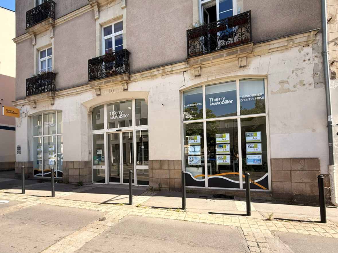 Façade d'une agence immobilière avec vitrine commerciale et accès PMR en rez-de-chaussée d'un immeuble en pierre