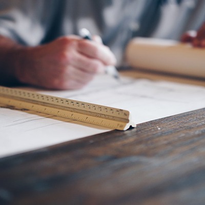 Gros plan sur une main d'architecte utilisant une règle graduée sur des plans de construction immobilière