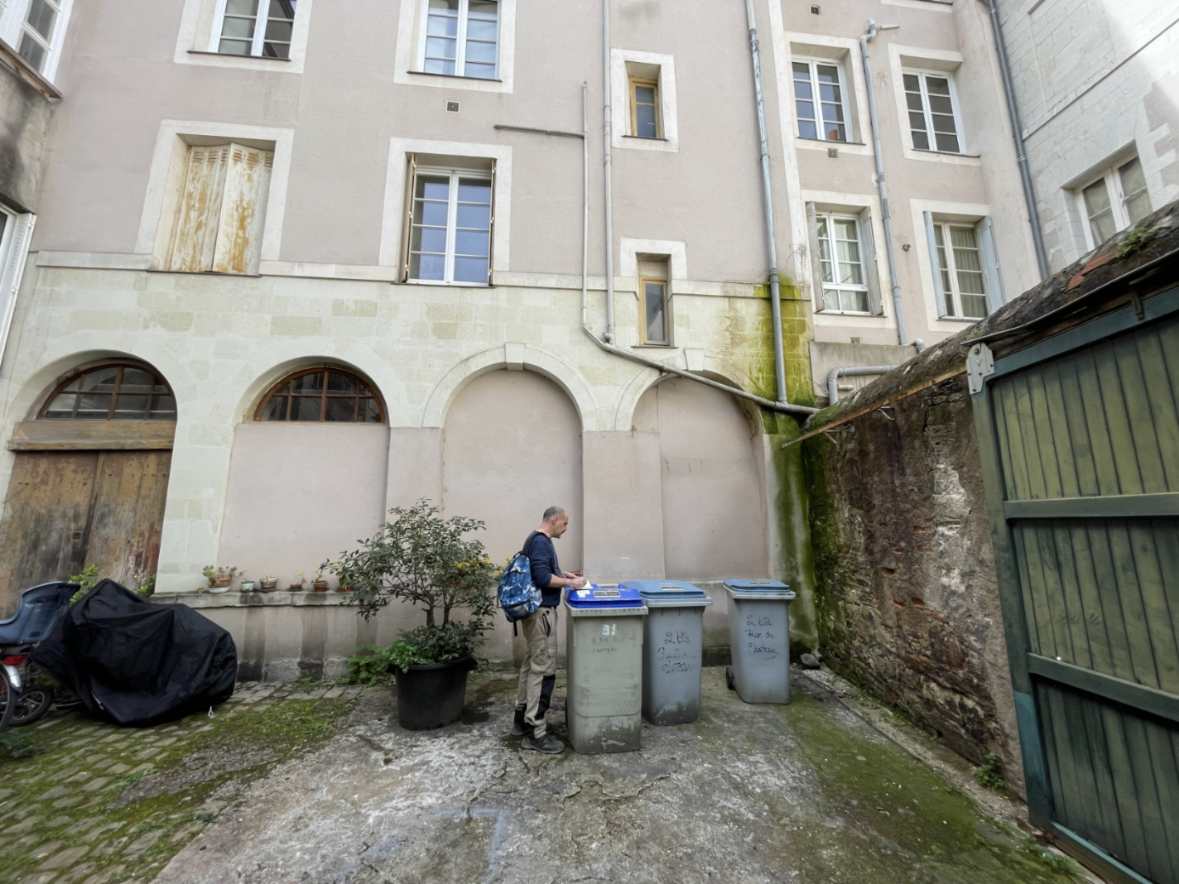 Un homme dépose des déchets dans des conteneurs de tri dans une cour intérieure pavée d'un immeuble ancien