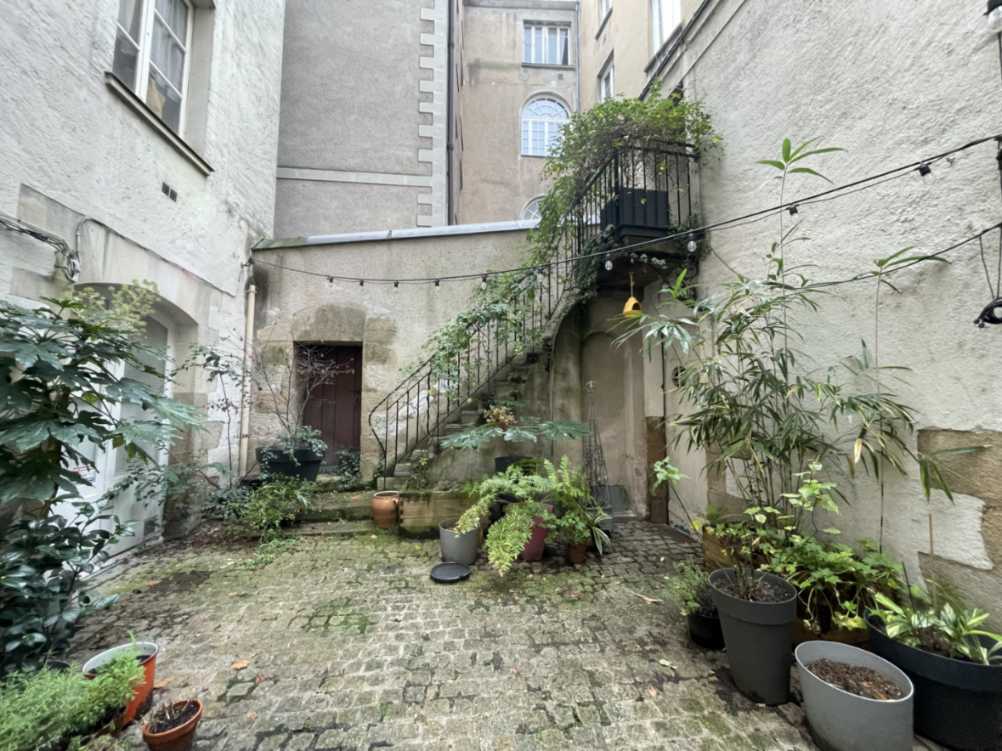 Cour intérieure pavée ancienne avec escalier extérieur en fer forgé, pots de plantes et murs en pierre