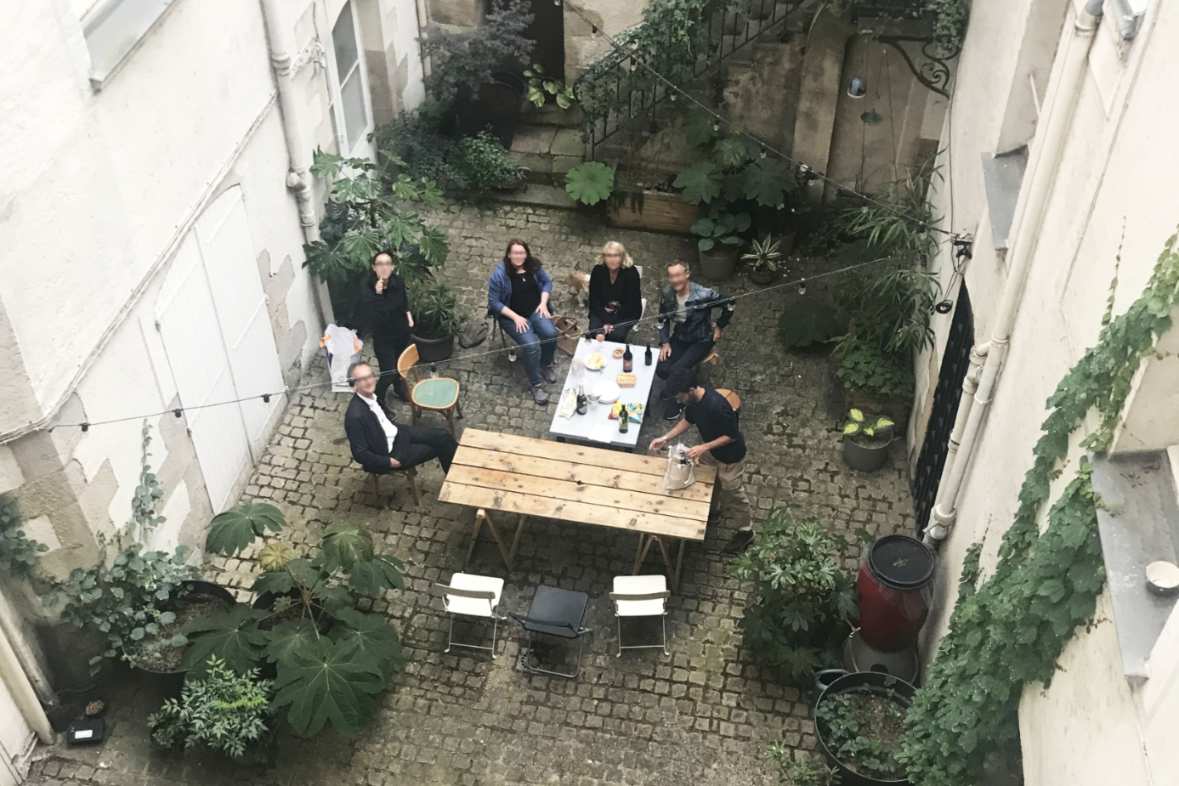 Vue plongeante sur une cour intérieure pavée avec végétation et groupe de personnes attablées