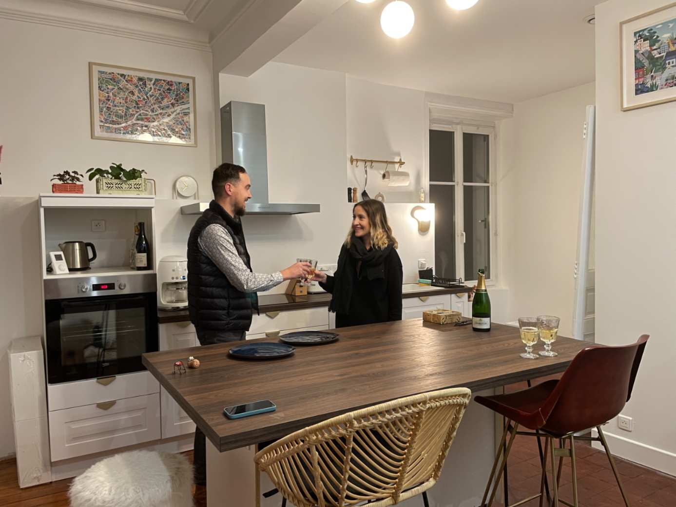 Cuisine blanche équipée avec îlot central en bois et couple trinquant, vue intérieure d'un appartement