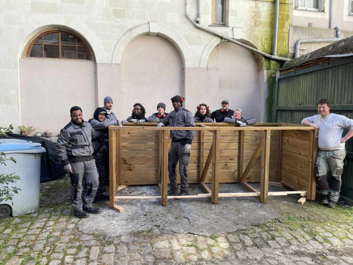 Équipe technique posant avec une structure de composteurs en bois récemment installée dans une cour intérieure