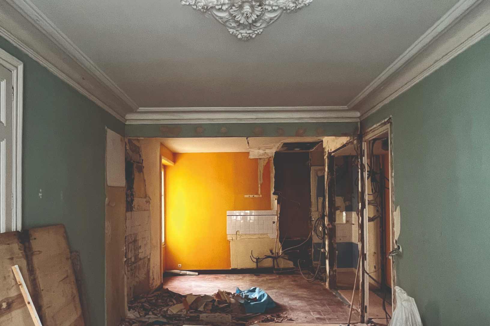 Intérieur d'un appartement en cours de démolition avec murs colorés et moulures au plafond