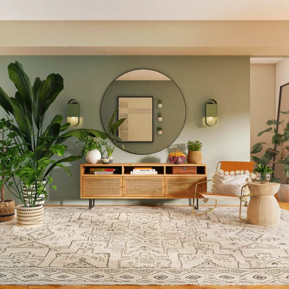 Intérieur de salon avec mur vert sauge, buffet en bois et rotin, grand miroir rond et plantes d'intérieur